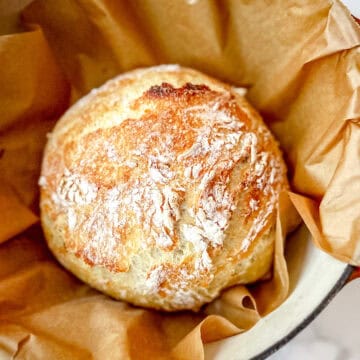 Baked No Knead Country bread on top of parchment paper in a dutch oven