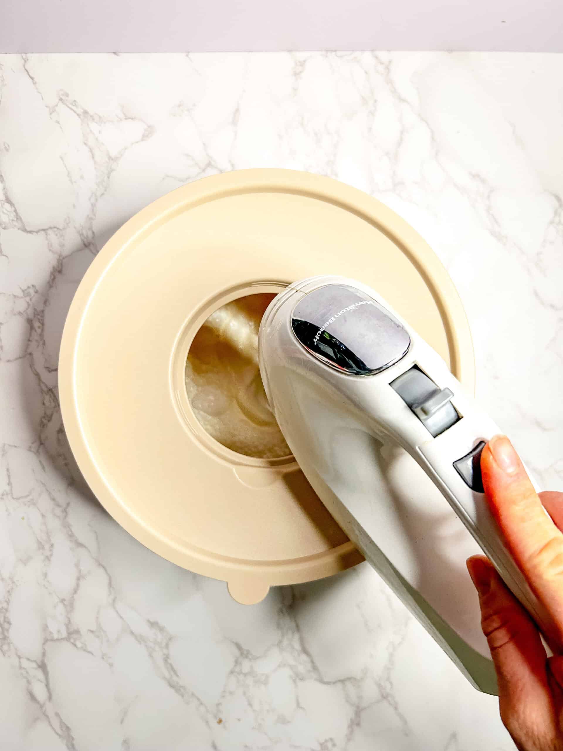 Mixing bowl covered and a hand mixer mixing the cream