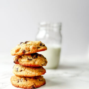 4 fresh milled flour sourdough cookies stack on top of eachother vertically with a mason jar of milk in the background