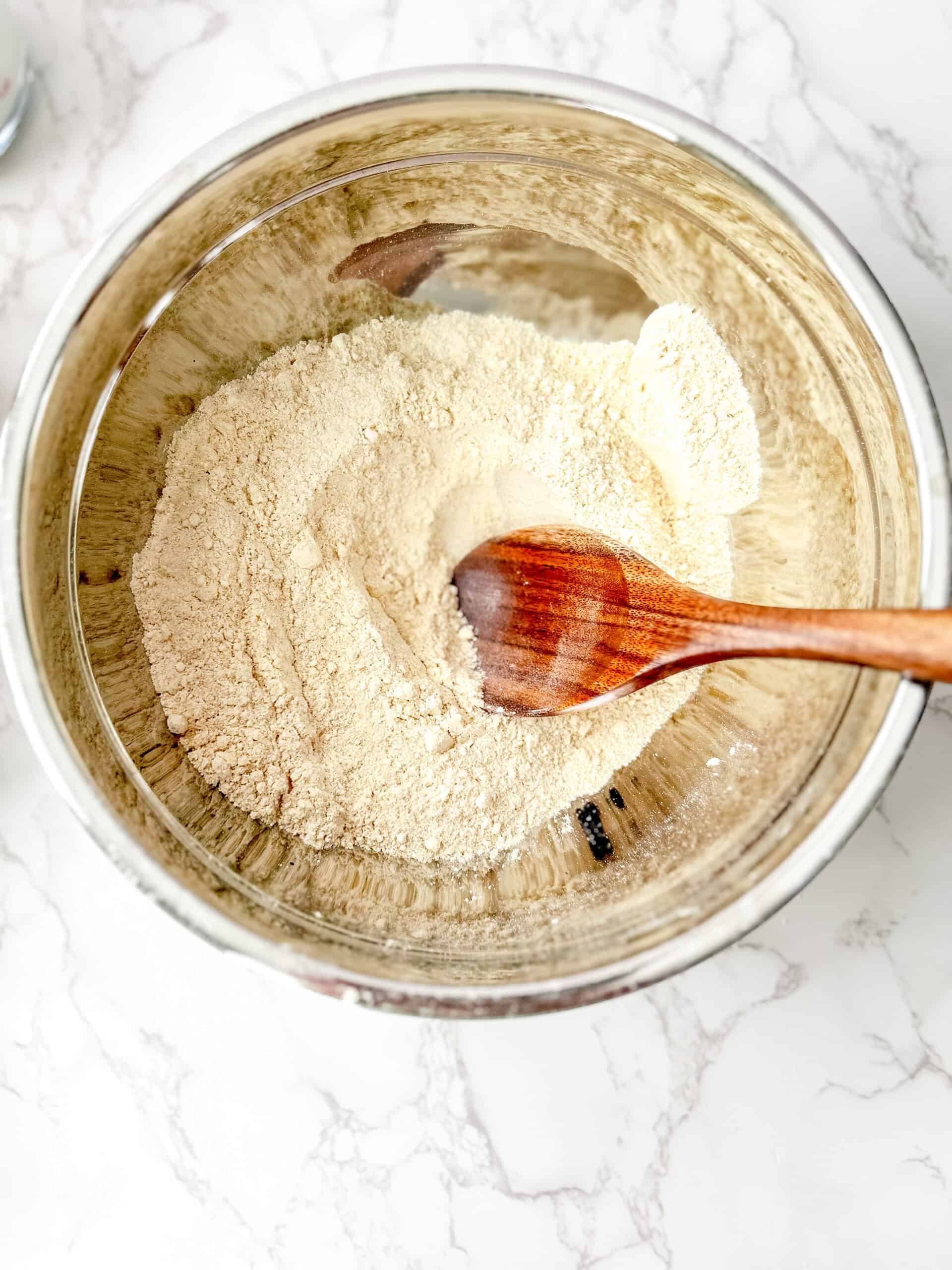 Dry ingredients mixed together in a large mixing bowl with a wooden spoon